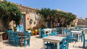 An outdoor café with blue and white tables and chairs, surrounded by stone walls and potted plants. - Red-house near the beach and with  (Avola-Siracusa)