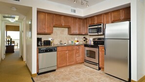 A modern kitchen with wooden cabinets, stainless steel appliances, and a tiled floor. - Coconut Cove All-suite (Clearwater Beach)