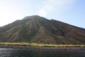 A mountain with a rocky foreground and a body of water. - Stromboli, At Nino's House (Stromboli)