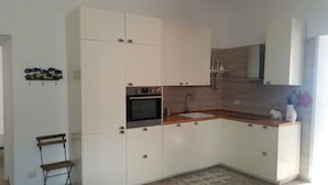 Una cocina moderna con armarios blancos, horno integrado, lavamanos y encimera de madera.