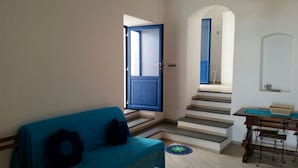 Una habitación con un sofá azul, una mesita con una cesta y una escalera que lleva a otra habitación.