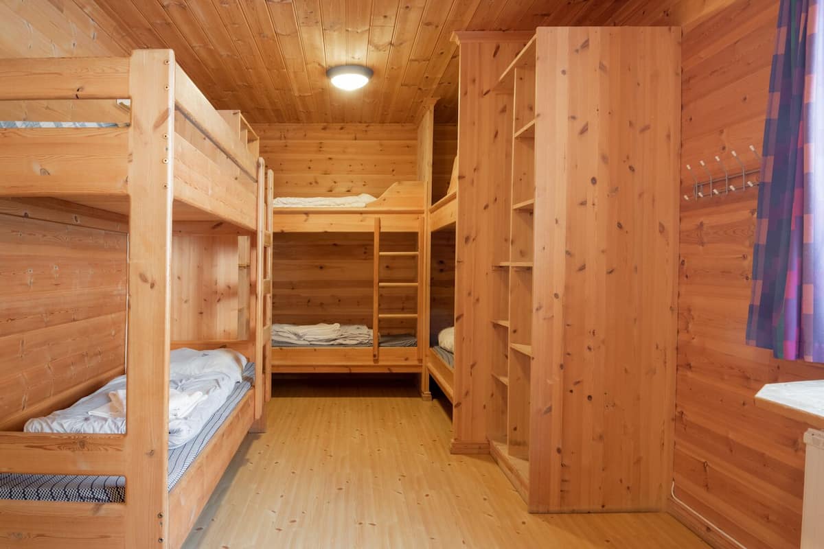 Une cabane en bois avec des lits superposés, des étagères intégrées et un luminaire central.