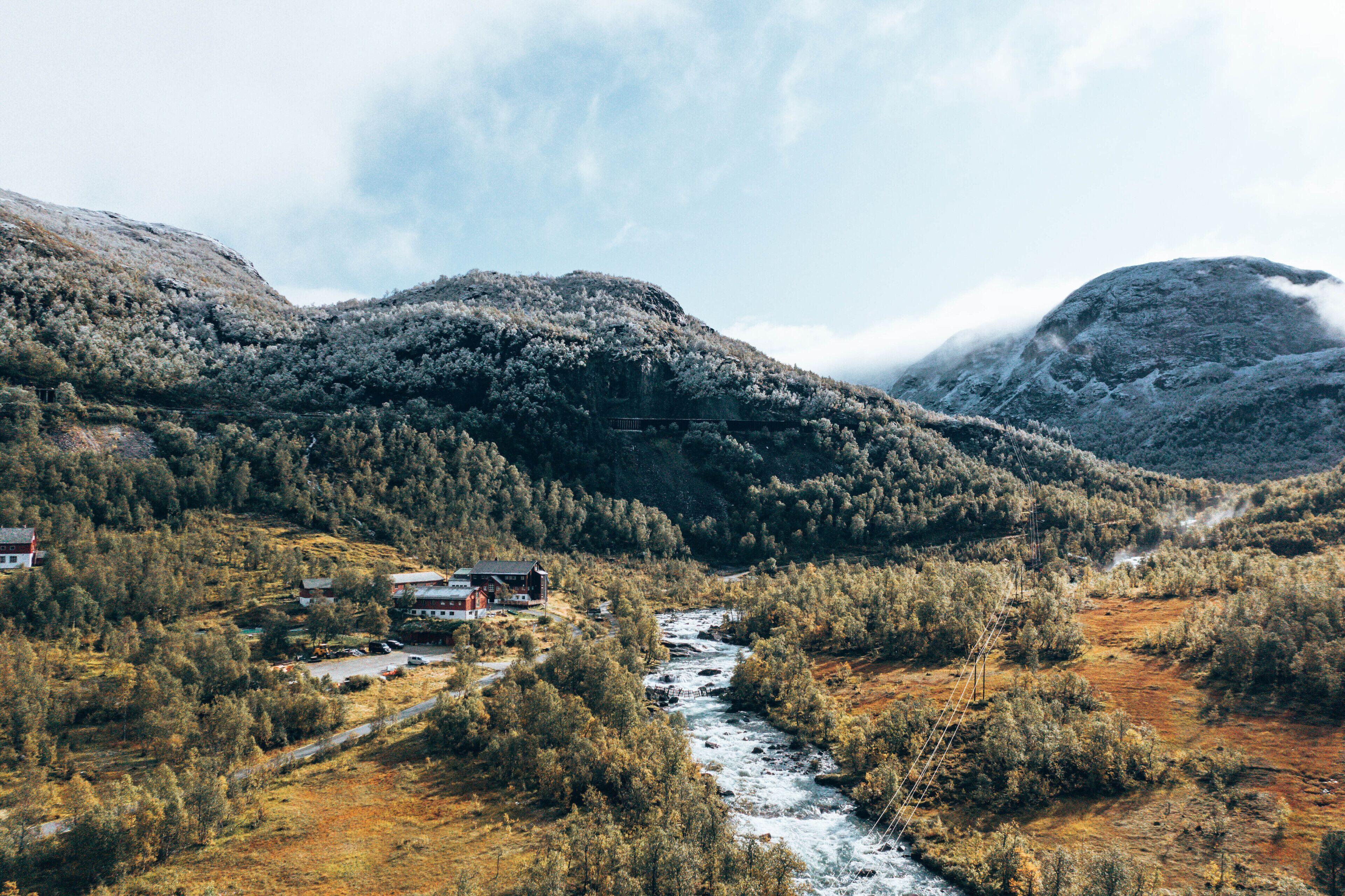 A mountainous landscape with a river, a bridge, and a building with a red roof.