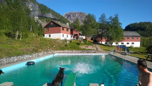 Una piscina con plataforma de madera, rodeada de casas y montañas al fondo.