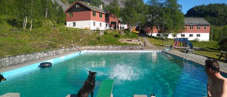 Una piscina con plataforma de madera, rodeada de casas y montañas al fondo.