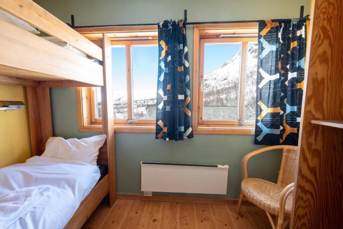 Une petite pièce de cabine comprenant un lit superposé, un lit simple, une chaise et une fenêtre avec des rideaux.