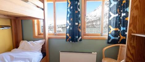 Una habitación de cabaña pequeña con una litera, una cama individual, una silla y una ventana con cortinas.