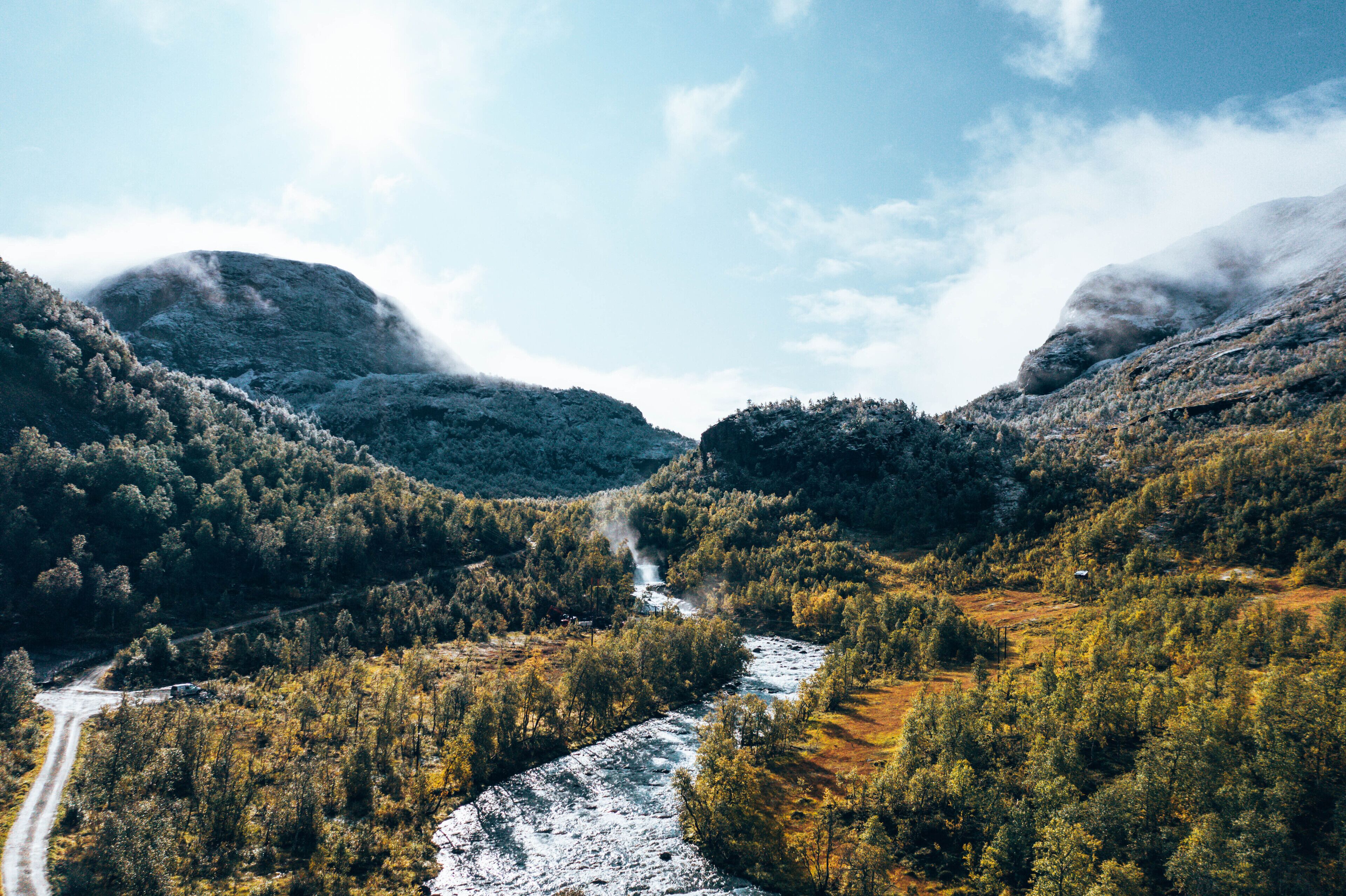 Een bergachtig landschap met een rivier, dicht bos en een onverharde weg.
