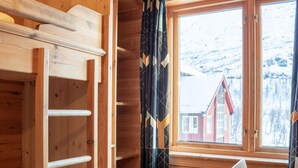 Habitación de cabaña de madera con literas, una ventana con cortinas, un radiador y una silla.