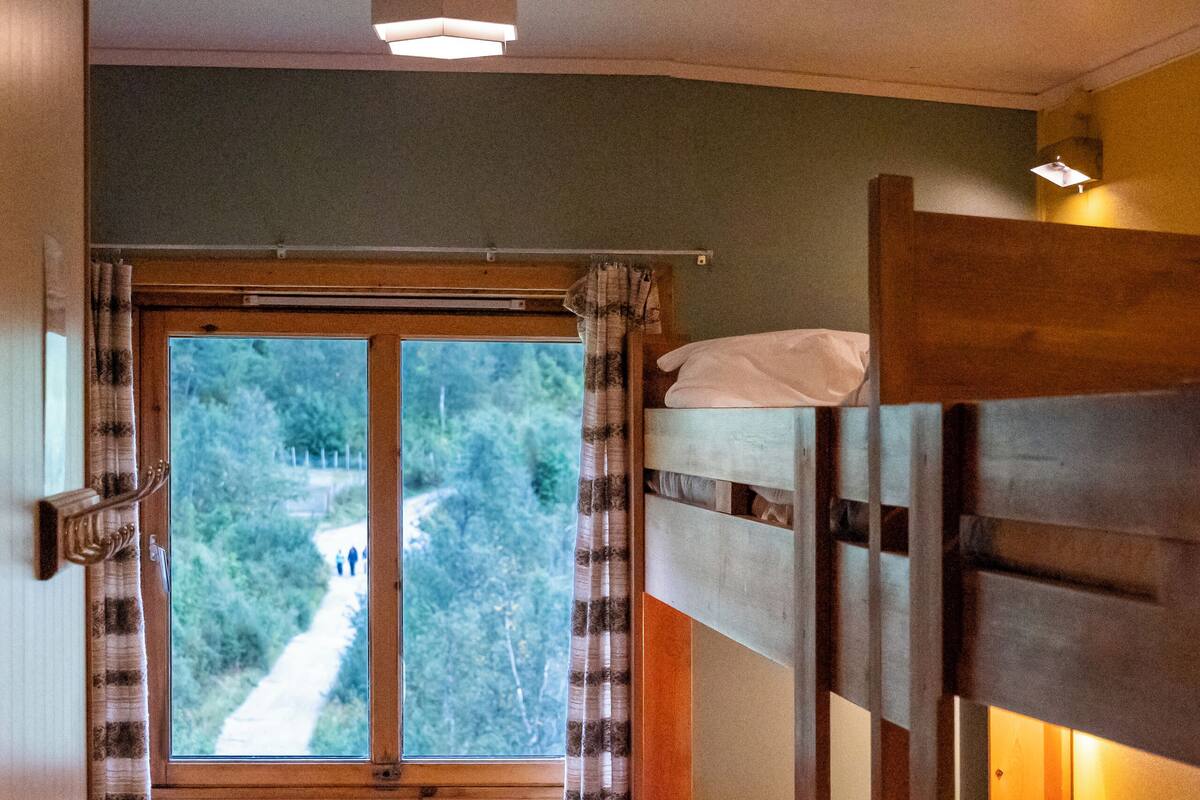 Une chambre avec un lit superposé et une fenêtre donnant sur un sentier.