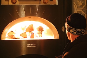 A pizza oven with the label "ALFA PIZZA made in Italy" and a person in the foreground. - Mjølfjell Ungdomsherberge (Voss)