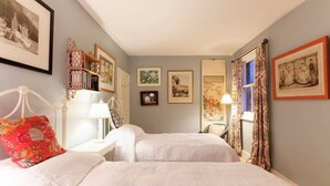 Una habitación con dos camas, una mesita de noche, una lámpara y cuadros en las paredes.