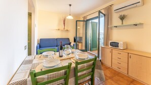 A dining area with a table set for four, a sofa, a microwave, and an air conditioning unit. - One bedroom apartment (4 people) - Residence I Mirti Bianchi (Santa Teresa Gallura)