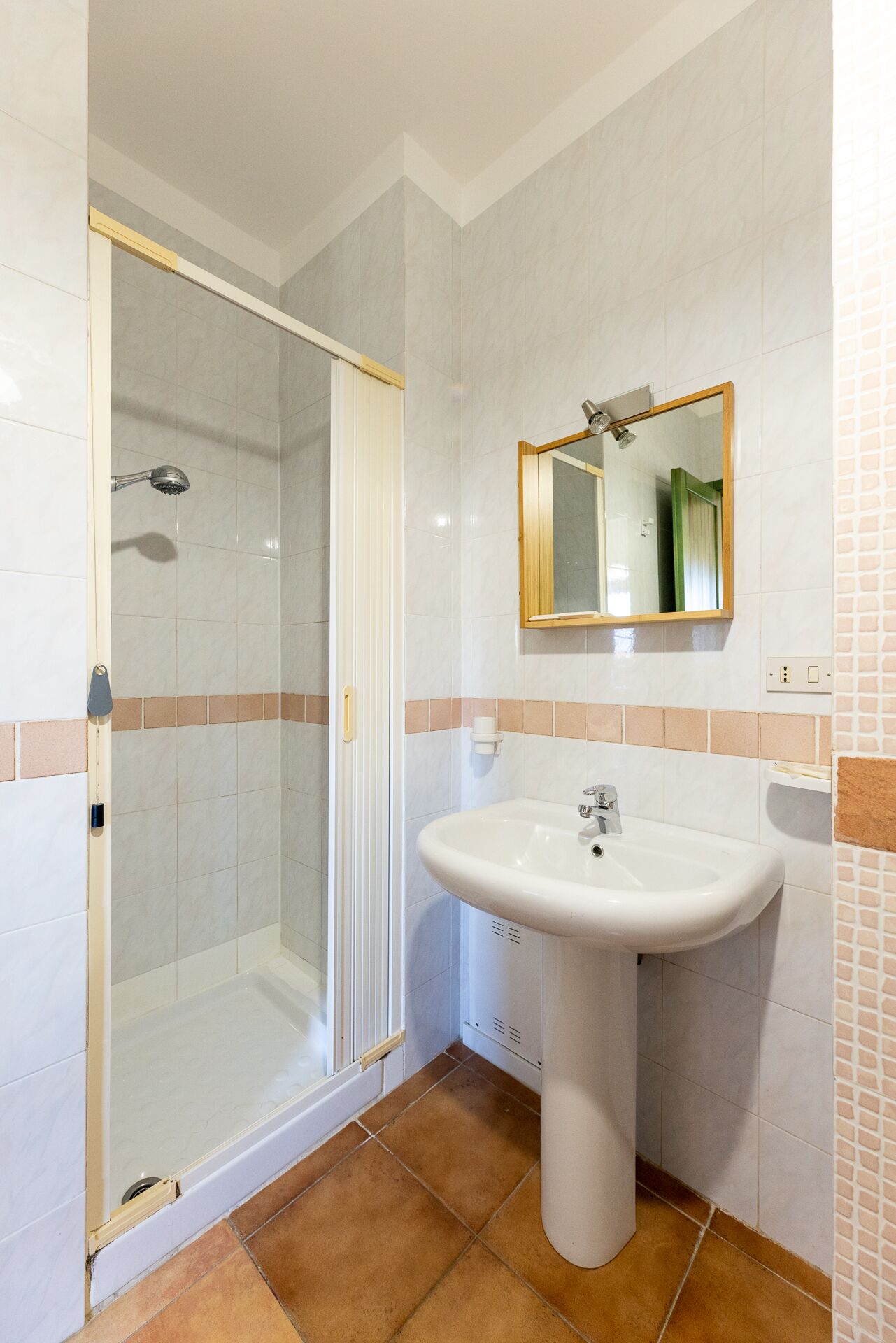 A bathroom with a glass shower enclosure, a pedestal sink, and a mirror above it.