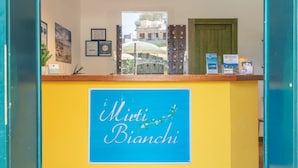 A reception desk with a sign reading "Miti Bianchi" and various informational posters and keychains. - One bedroom apartment (4 people) - Residence I Mirti Bianchi (Santa Teresa Gallura)