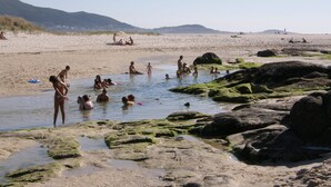 A beach with people swimming and relaxing in the water, surrounded by rocks and mountains in the background. - Apartment/ flat - Coruña (O Pindo)
