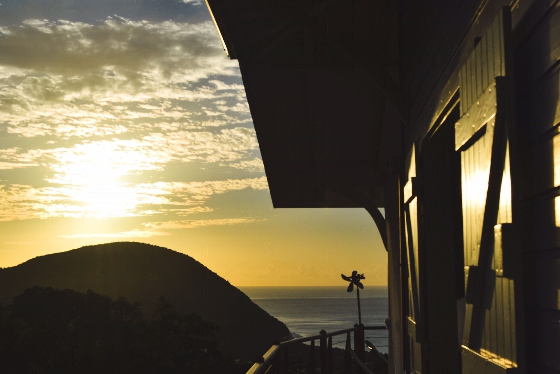 A sunset view from a balcony overlooking the ocean, with a mountain in the background.