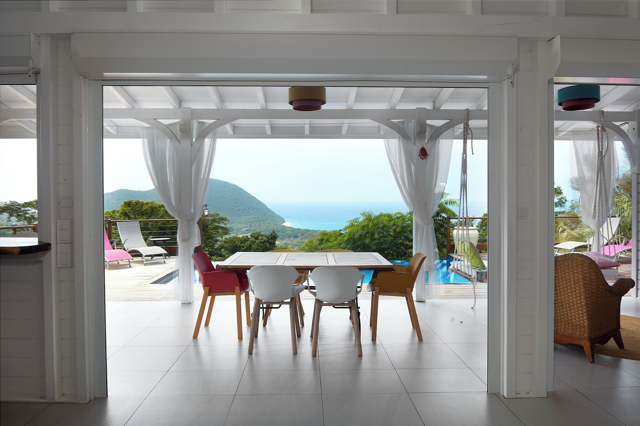 A dining area with a table and chairs, a view of the sea and mountains, and a pool in the background.
