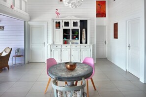 Een eethoek met een ronde tafel, twee stoelen, een witte kast met glazen deuren en een roze flamingo decoratie.