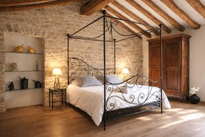 Un lit à baldaquin avec un mur en pierre en arrière-plan, un plancher en bois et une armoire en bois sur le côté droit.