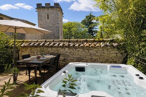 A hot tub in a stone-walled outdoor area with a table and chairs set up for dining. - Charming detached house for 2 with private jacuzzi. Prestige & design. (Carnas)