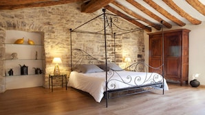 A bedroom with a four-poster bed, stone walls, wooden beams, a nightstand with a lamp, and a wooden cabinet. - Charming detached house for 2 with private jacuzzi. Prestige & design. (Carnas)