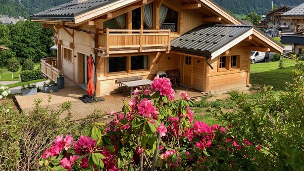A wooden chalet with a balcony, a covered patio, and a view of the surrounding mountains.