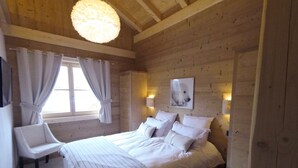 A wooden-paneled bedroom with a large bed, a chair, and a window with curtains.