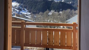 A wooden balcony with a view of snow-covered mountains and forested valleys.