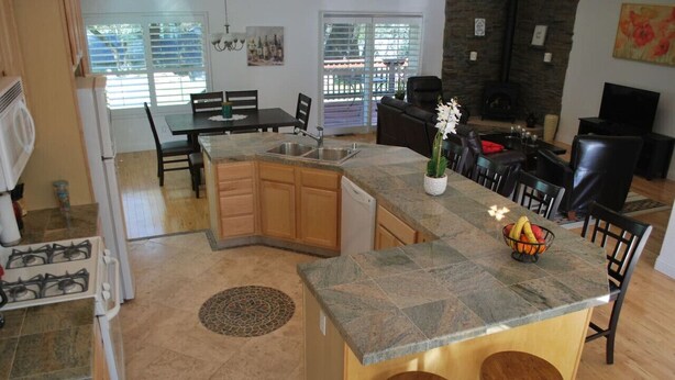 A kitchen with a granite countertop, wooden cabinets, and a built-in island with stools.