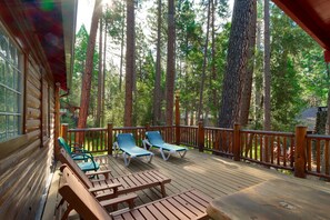 A wooden deck with lounge chairs and a table, surrounded by tall trees.
