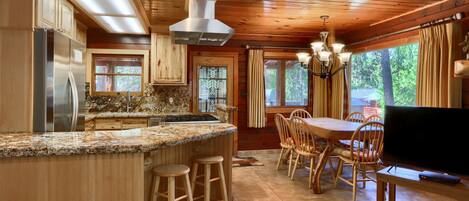 Una cocina con una isla central, armarios de madera, un refrigerador de acero inoxidable y una zona de comedor con una mesa y sillas.