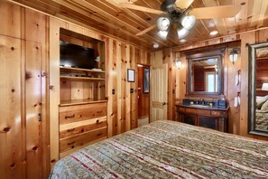 A wooden room with a bed, a television, and a bathroom with a mirror and sink.
