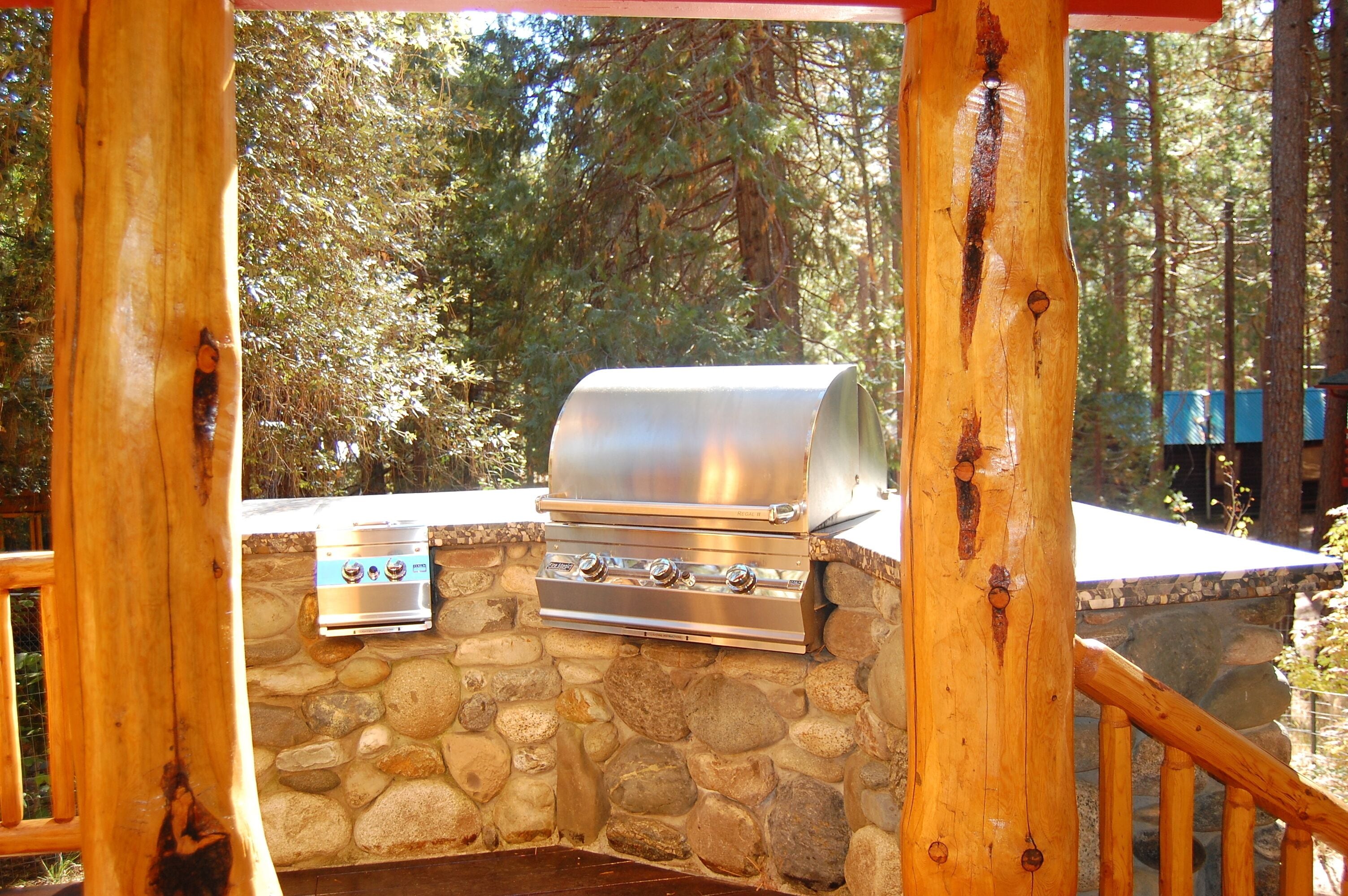 An outdoor grill setup with a stone wall and wooden posts.