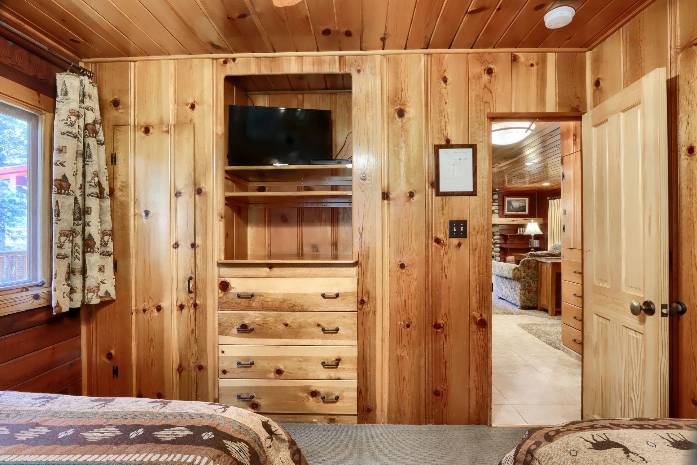 A wooden room with a bed, a TV on a shelf, and a door leading to another room.