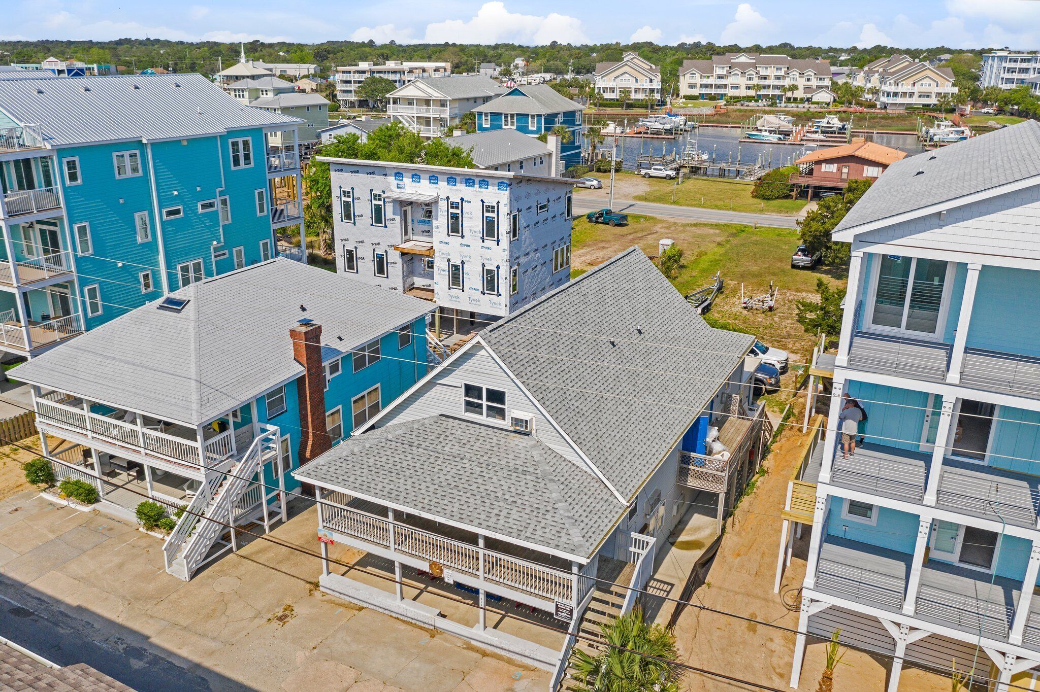 Ett bostadsområde vid kusten med flera tvåvåningshus, vissa med balkonger och några med synliga byggnadsställningar.
