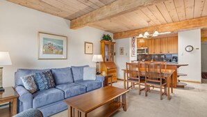 Una sala de estar con un sofá azul, una mesa de centro de madera y una zona de comedor con sillas y una mesa de madera.