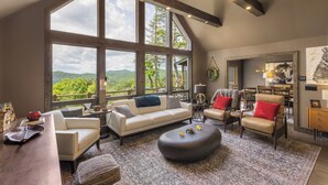 A spacious living room with a large window, a sofa, a coffee table, and a fireplace. - Bella Vista - Views! Views! Views! (Highlands)
