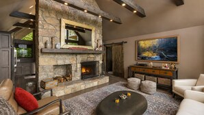A stone fireplace with a TV above it, a large painting on the wall, and a cozy seating area with a leather sofa and ottoman. - Bella Vista - Views! Views! Views! (Highlands)