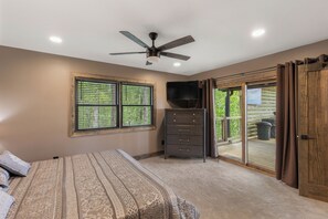 Une chambre avec un lit, un ventilateur de plafond, une commode, un téléviseur et une porte-fenêtre coulissante donnant sur un espace extérieur.