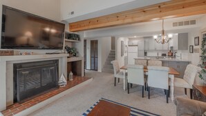 A modern living room with a fireplace, a television, and a dining area with a kitchen in the background. - The Lions Den Pt. II by Innsbrook Vacations! (Innsbrook)
