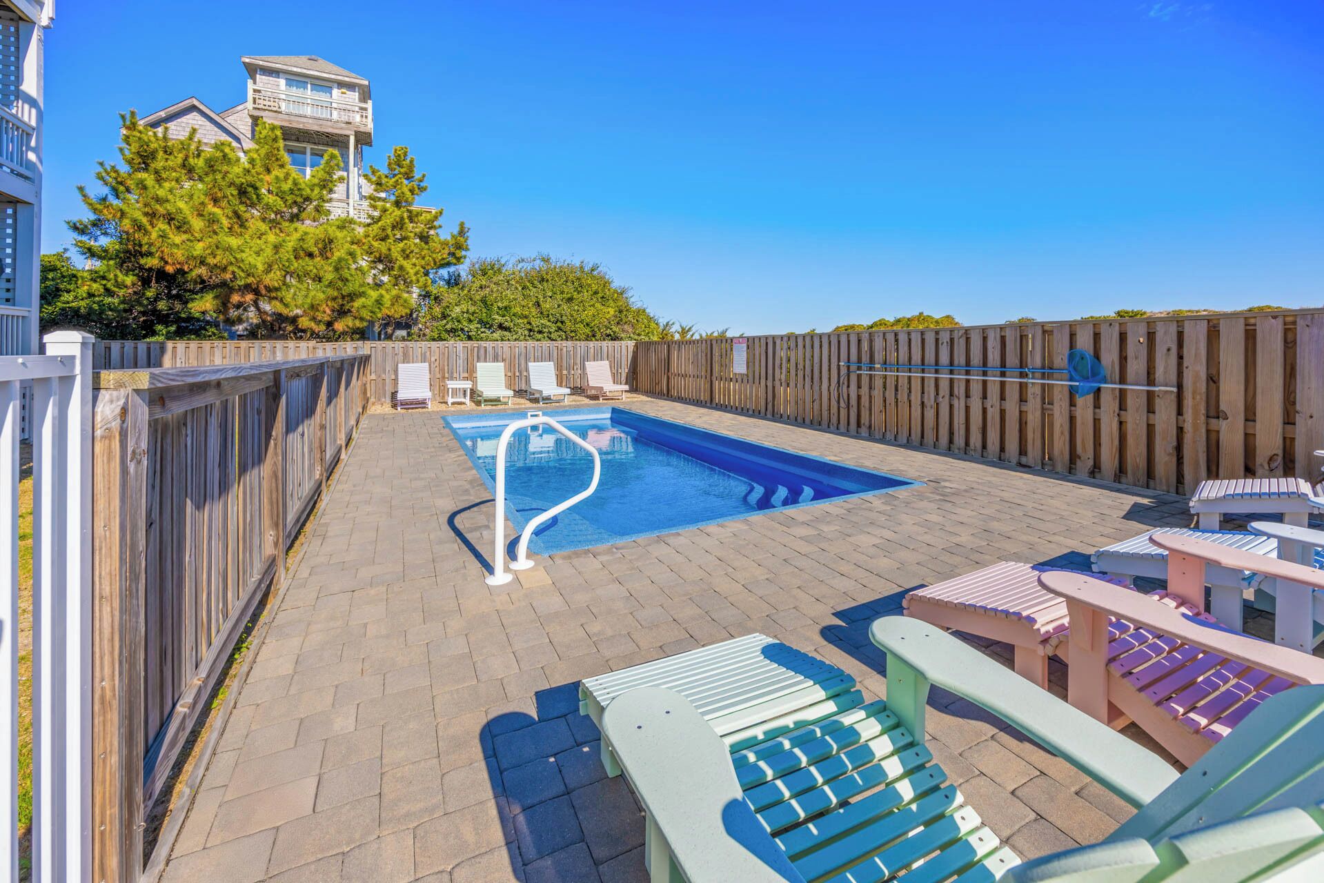 Um quintal com piscina, espreguiçadeiras e cerca de madeira.