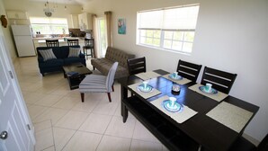Amplia sala de estar con un comedor de madera oscura listo para cuatro personas, un sofá y una cocina al fondo.