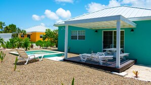 Una casa con patio cubierto, piscina y un pequeño jardín.