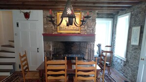A dining area with a wooden table and chairs, a bowl of fruit, a stone fireplace, and a chandelier. - New Hope area Historical Bucks County Stone House circa 1732 (Lumberville)