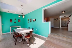 Una zona de menjador amb taula i cadires blanques, parets color cel i una escala que mena a una altra habitació.