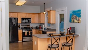 A modern kitchen with wooden cabinets, a black refrigerator, a stove, and a sink. There are two bar stools and a painting on the wall. - Large 3 BR 2.5BA Lake Norman House in Birkdale Village,Close to Charlotte! (Huntersville)