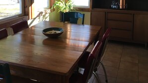 Zona pranzo con tavolo in legno, sedie, ventola a soffitto e finestra con tenda a quadri.