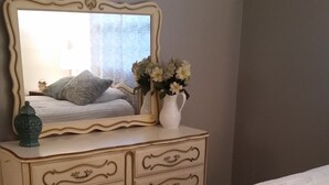 Un dormitorio con una cama, un tocador con espejo y un florero con flores.