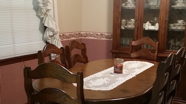 Un comedor con una mesa de madera, sillas, un aparador con puertas de cristal y una ventana con cortinas.